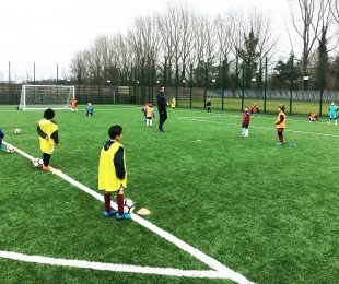 Children dribbling with footballs on the pitch