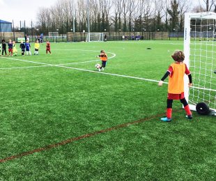 Child kicking a football doing a penalty shootout on the 4k weather pitch